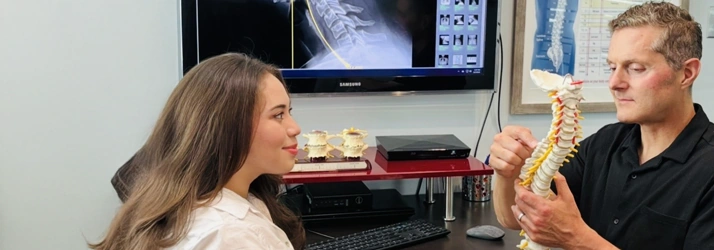 James Roeder holding a spine model while speaking with a patient in an examination room.