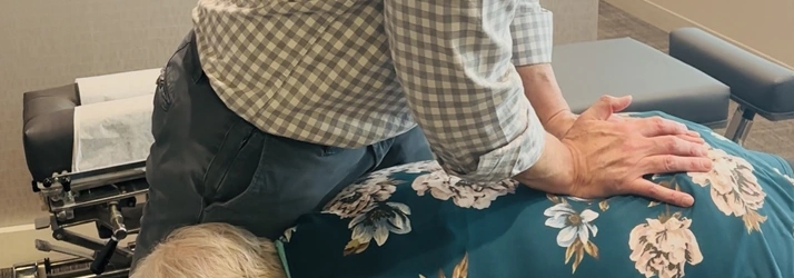 Hands pressing along the back of a patient wearing a floral shirt.