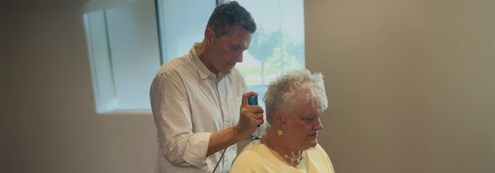 James Roeder using a handheld instrument near an older patient's head while she lies on a treatment table.
